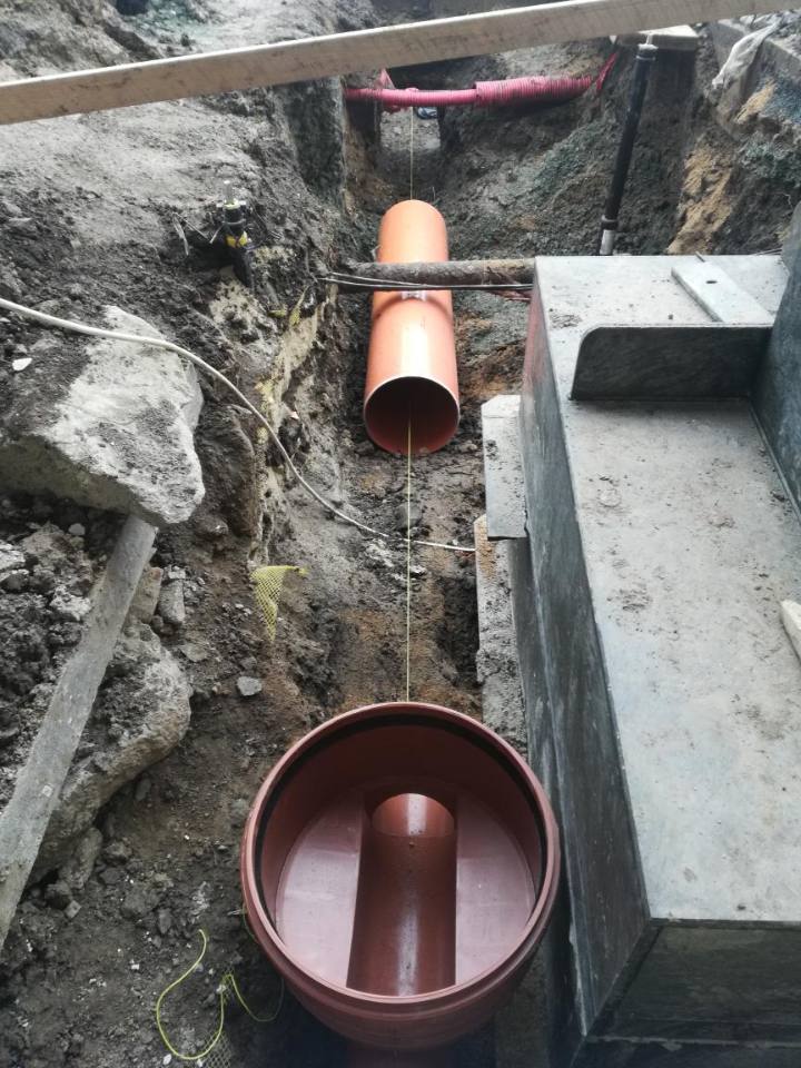 Dno plastové revizní šachty a oranžové potrubí kanalizační přípojky ve výkopu