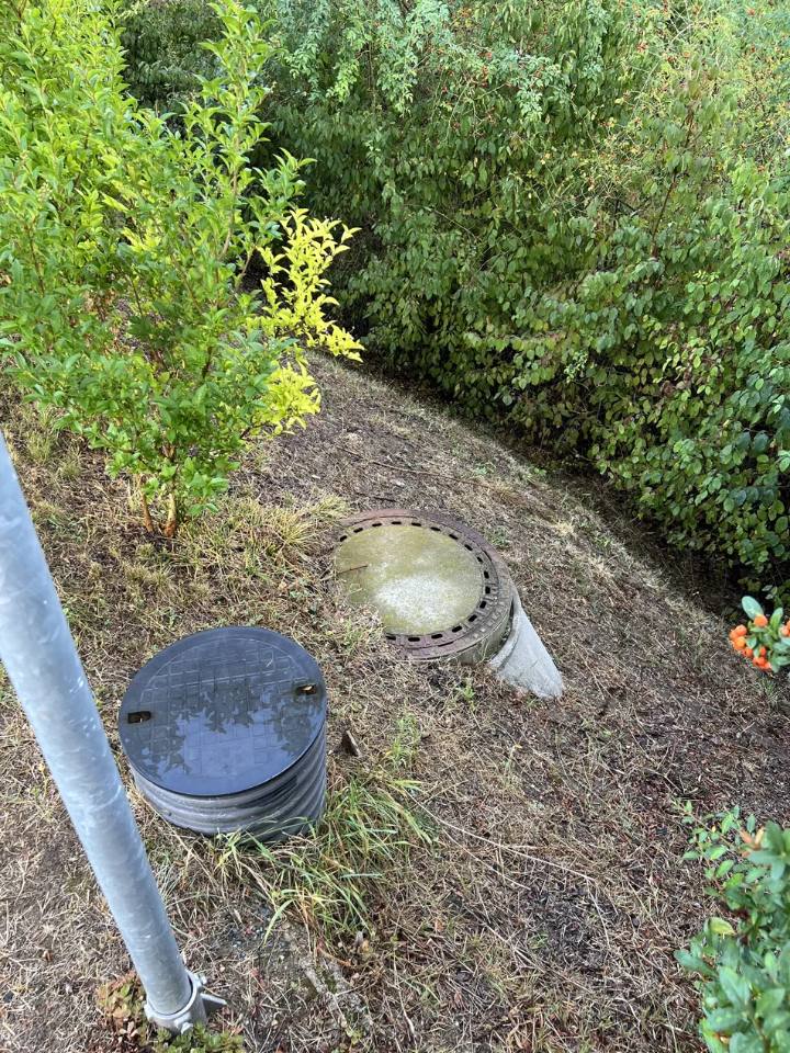 Plastová a betonová kanalizační šachta s poklopy na travnatém pozemku